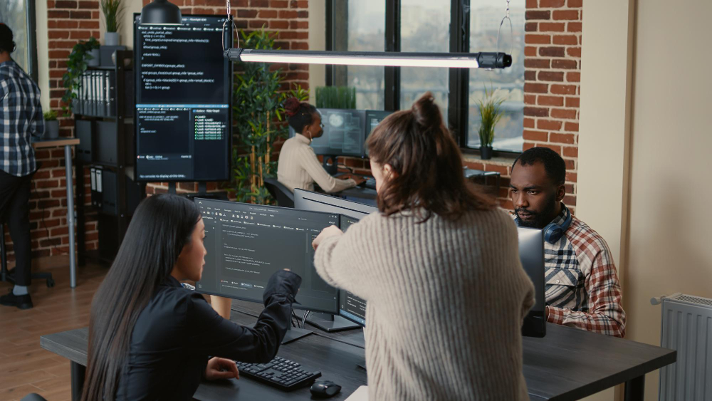 software-programer-pointing-pencil-source-code-computer-screen-explaining-algorithm-coworker-standing-desk-programmers-discussing-online-cloud-computing-with-team